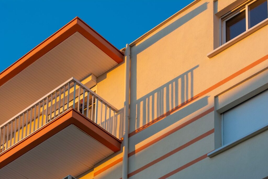 Close-up of a modern apartment building facade featuring balconies and striking sunlit shadows.