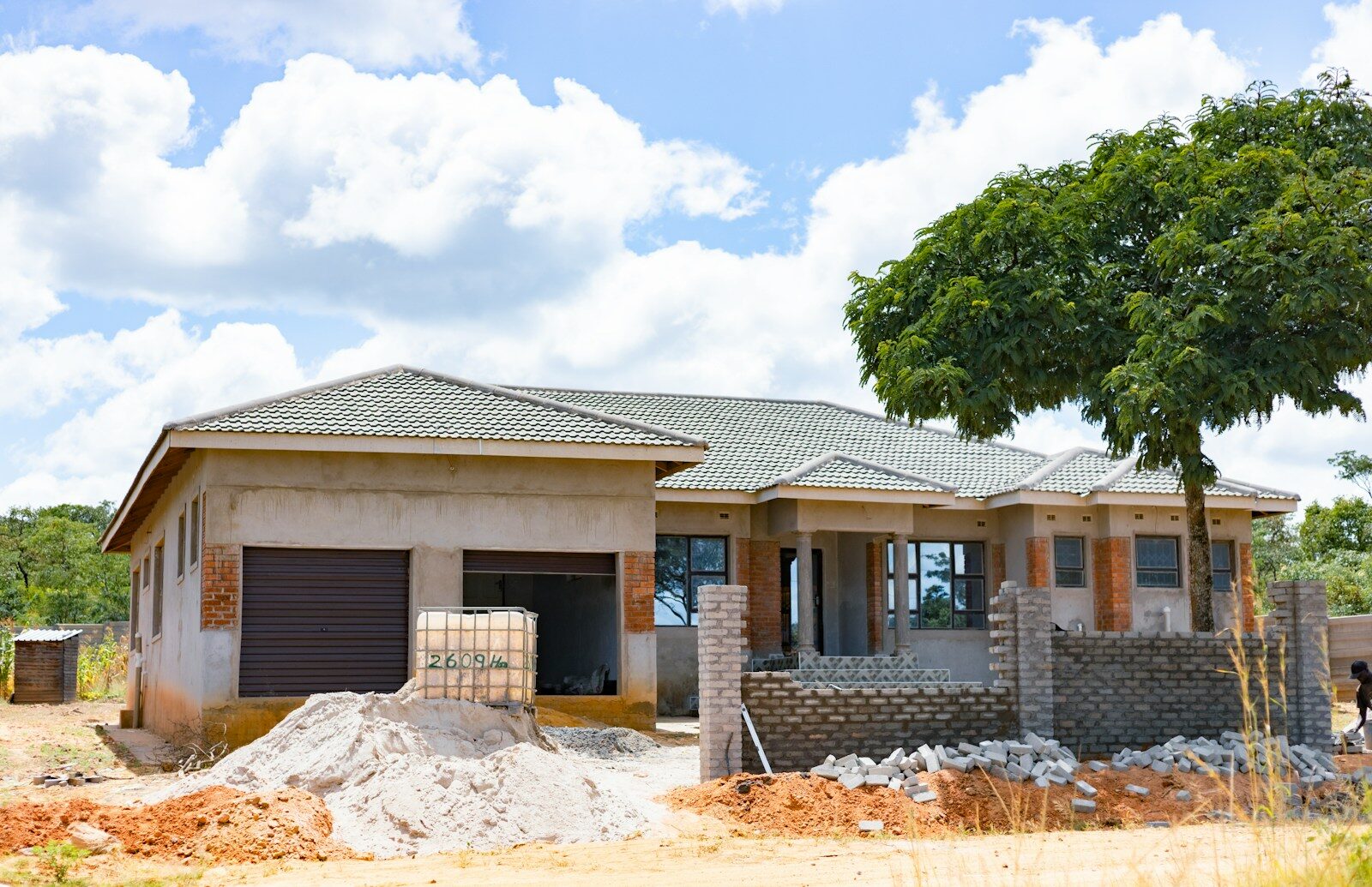 A house under construction with a tiled roof and brick accents near a tree